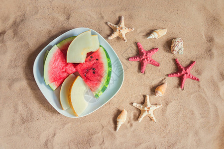 在沙滩上放着甜瓜和西瓜片海星和贝壳的盘子图片