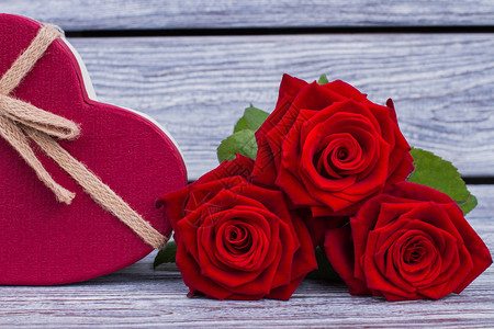 三朵红玫瑰和木制背景上的心形礼品盒图片