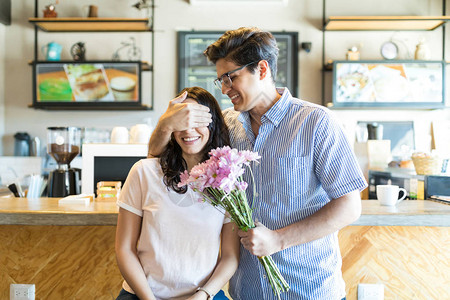 快乐的年轻男人在咖啡馆拿着花束时遮图片