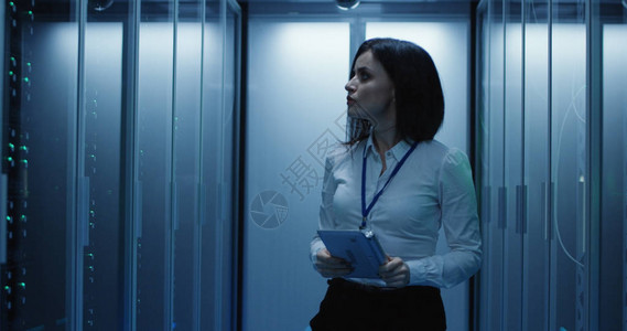在一个充满机架服务器的数据中心使用平板电脑工作的女技术人员的中照图片