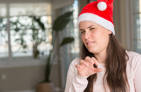 美丽的年轻女子在家里戴着圣诞老人帽子厌恶的表情图片