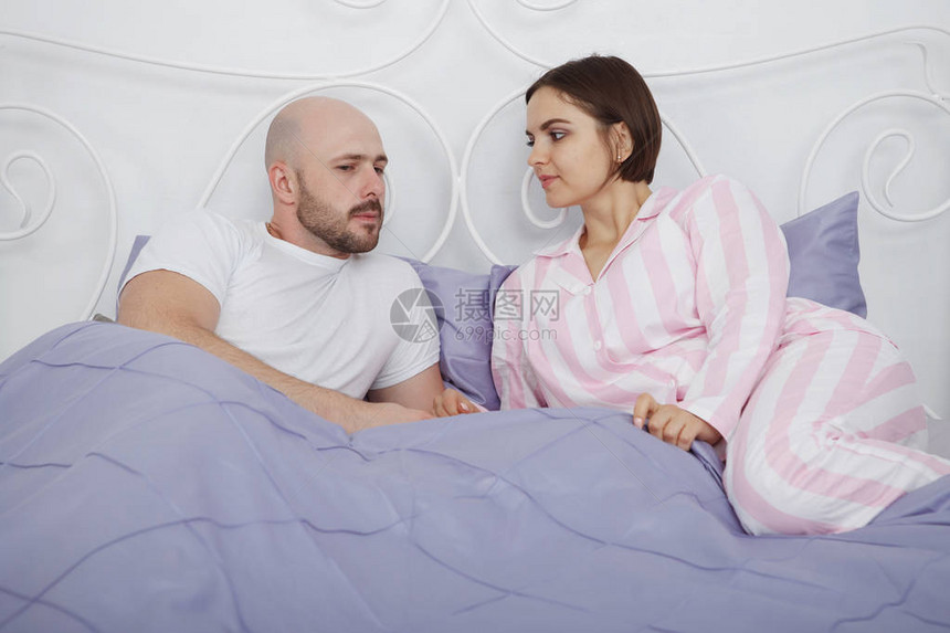 年轻漂亮女人和一个穿着睡衣拥抱的秃头胡子男人和枕头和蓝床图片