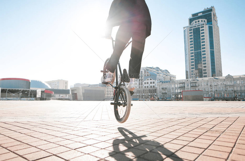 小轮车自由式BMX自行车手在自行车上做出复杂的技巧年轻人在城市广场的背景下制作图片
