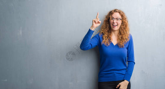 红发女青年在灰色的墙壁上指着成功的点子图片