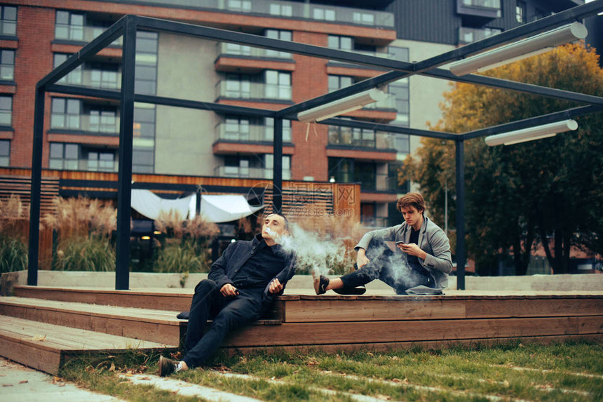 两个朋友坐在公园的长凳上友谊两个穿着大衣的时尚男士男人vape图片
