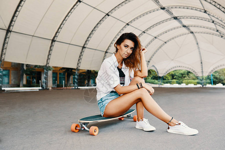 时尚都市女孩与Longboard合影在城市溜冰鞋的时髦女孩极限运图片