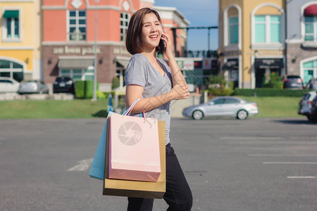美丽的年轻购物狂亚洲女人一边走路一边用智能手机说话图片