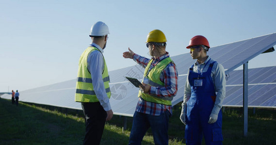 3名身穿反射背心的男电气工人中镜头在光伏太阳能电池板背景图片
