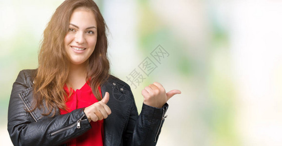 身穿时尚皮夹克背景孤立的漂亮大号年轻女用手和拇指向背后图片