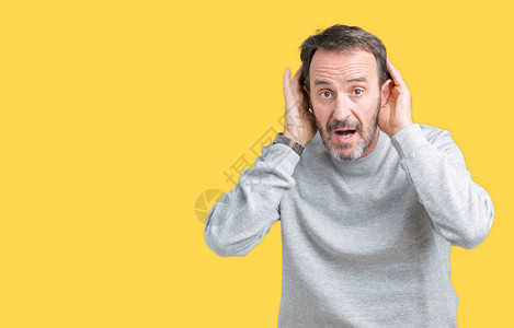 英俊的中年老人在孤立的背景下穿着运动衫试图听到双手在耳朵上的手势图片