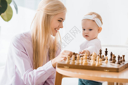 年轻快乐的母亲教女儿下象棋并给女图片