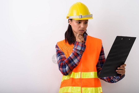年轻亚洲女建筑工人在剪贴板上阅读时用白种背景思考的片图片