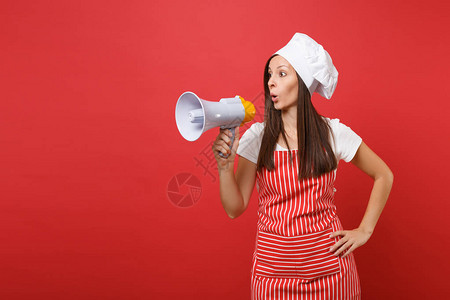 女主妇用条纹围裙白色T恤衫脱红墙背景孤立的厨师帽图片