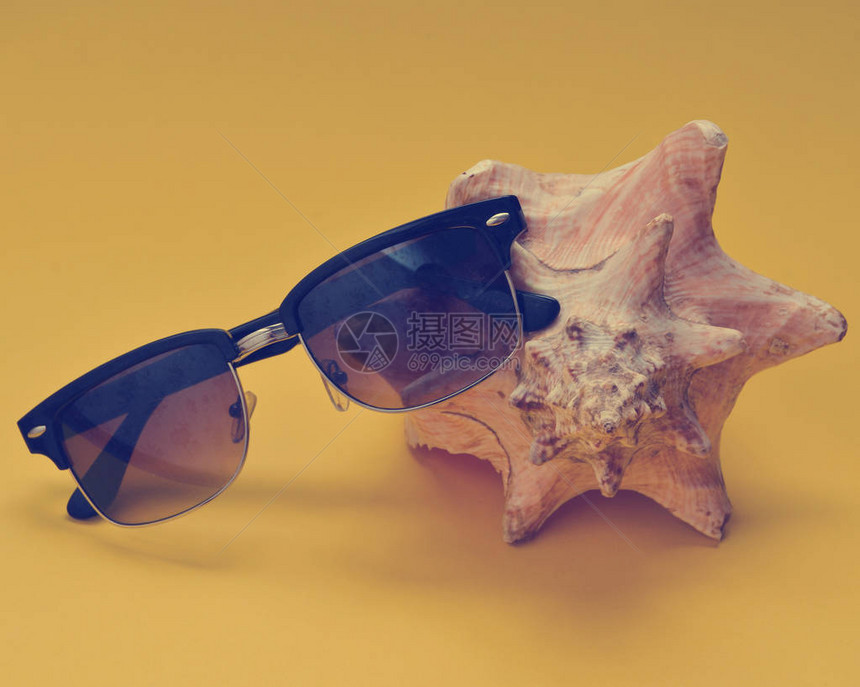黄色背景的巨型肌肉壳和太阳镜在沙滩上放松一下的概念图片