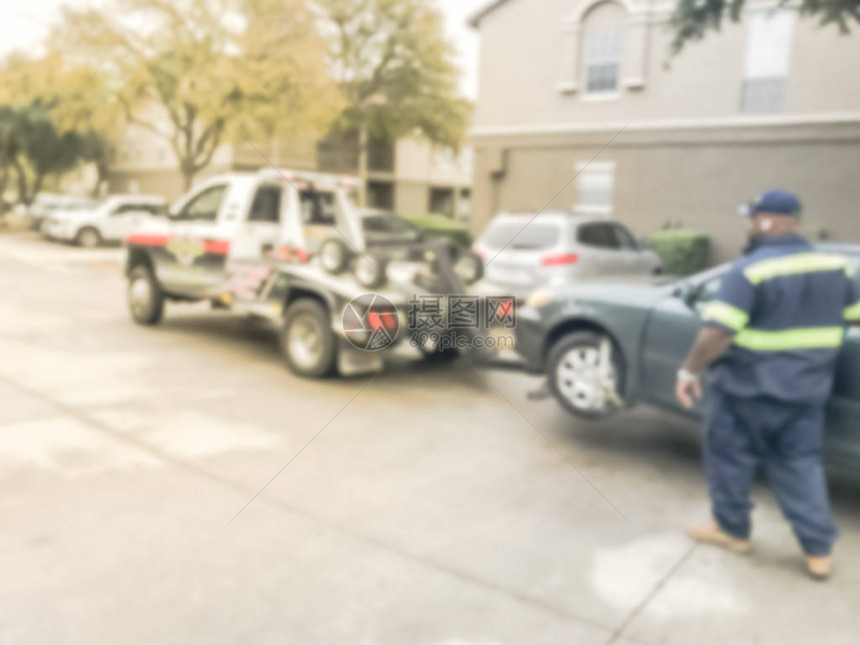 运动模糊的拖车司机从美国德克萨斯州的公寓大楼拖着一辆损坏的汽车图片