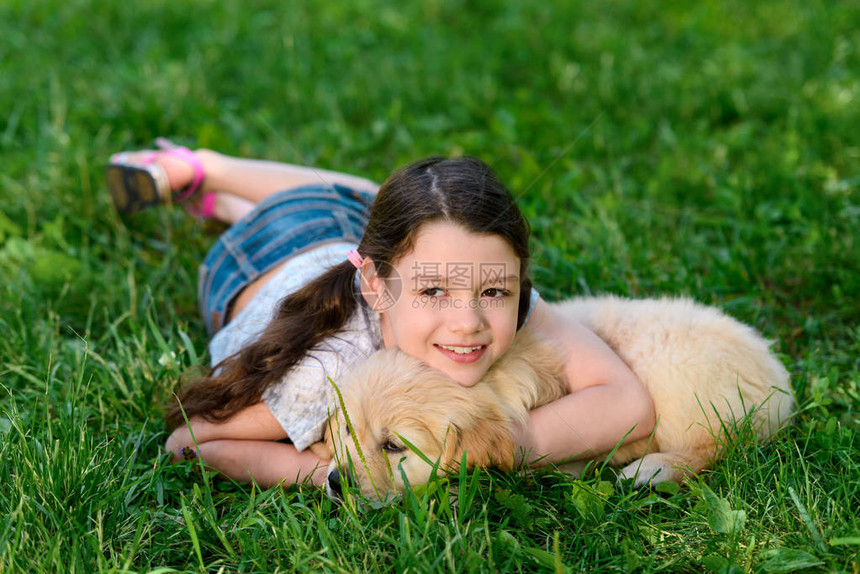 女孩和她的狗躺在草地上孩子拥抱小狗看图片