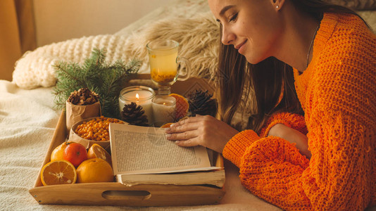 一张温暖的橙色毛衣在床上端着一杯茶和水果的女人的柔软舒适照片图片