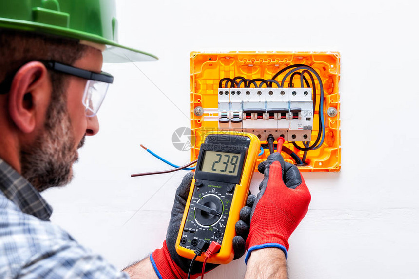 带头盔护目镜和手的电气技师在住宅电板上用手套测量电压图片