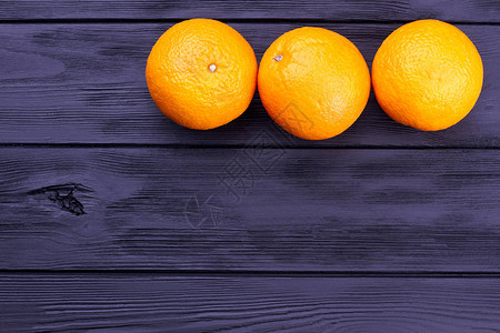 深色木制背景上的三个完整的橙子三个成熟的橙色水果行和复制空间橙子图片