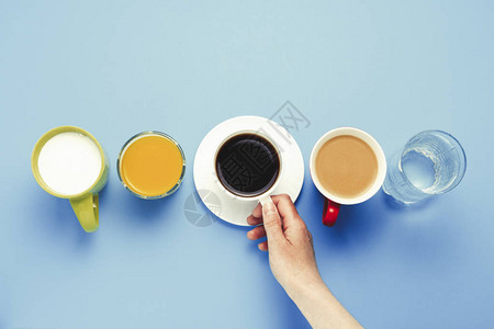 女手握着一杯黑咖啡和一组健康饮料橙汁卡布奇诺水蓝底酸奶图片