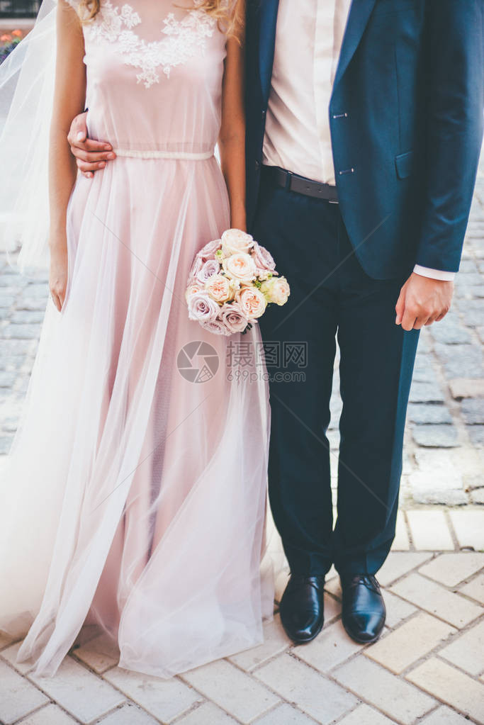 拥抱夫妇与新娘手中的奶油色玫瑰花卉婚礼花束新娘和新郎站立图片