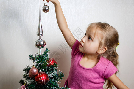 一个可爱的学龄前儿童准备在她小的圣诞树上放球图片