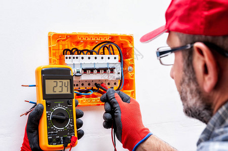 配有手套保护手的电工技师在住宅电板中测量电压单图片