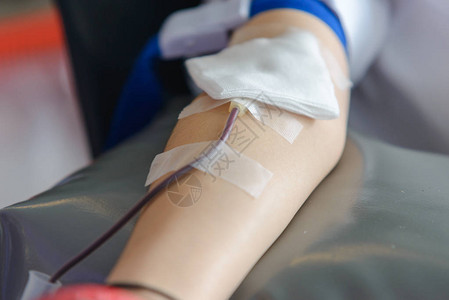 关闭亚洲男右臂接受血液并手持橡皮球医疗保健和慈善事业输血献背景