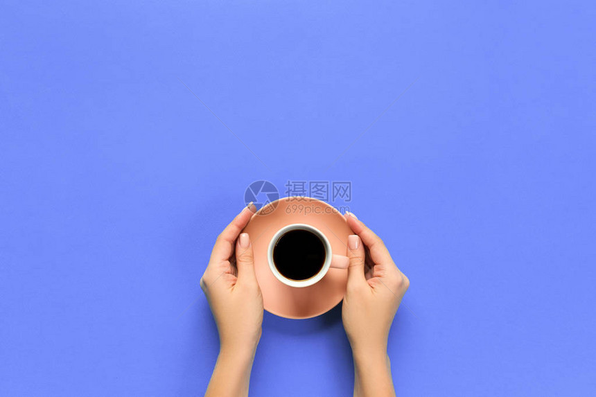 女手臂在紫色背景上握着咖啡杯顶端视图片