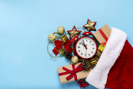 红色闹钟圣诞老人帽子圣诞树装饰品蓝色背景上的礼物图片