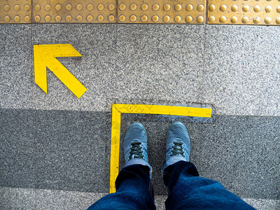 站在地铁站台上箭头符号的人脚的顶部视图火车站地板上的图片