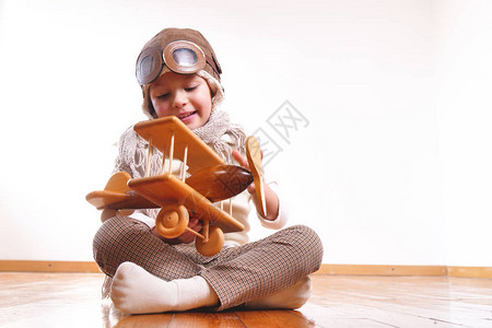 俏皮可爱的小女孩打扮成飞行员坐在木地板图片