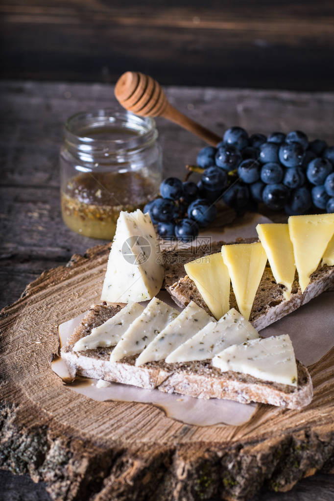 什锦奶酪配葡萄面包蜂蜜在深色木质背景上山羊奶酪配香草天然木板意大利开胃菜意式面包配奶酪静物的食图片