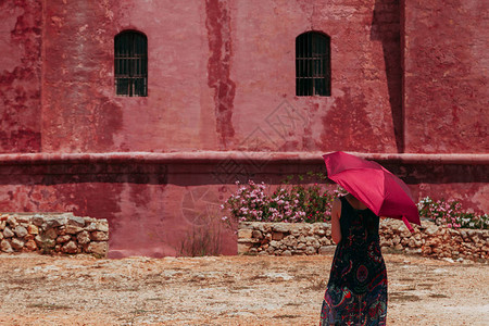 年轻寂寞的姑娘拿着红色雨伞保护自己免受太阳照射就在红古城图片