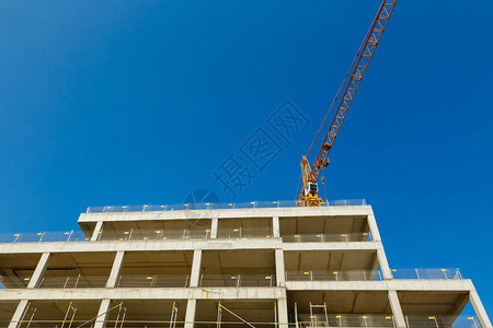 起重机和未完成的建筑在蓝天背景下建造公寓的房子图片