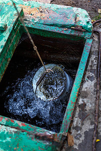 清洁水正用桶子从肮脏的破烂井里的图片