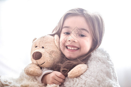 小可爱的小女孩拥抱泰迪熊玩具在光背景上图片