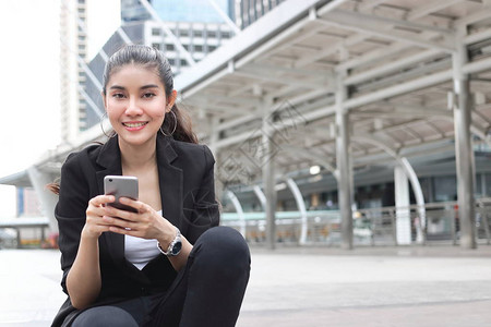 在城市背景中拥有移动智能手机的亚洲年轻女商人图片