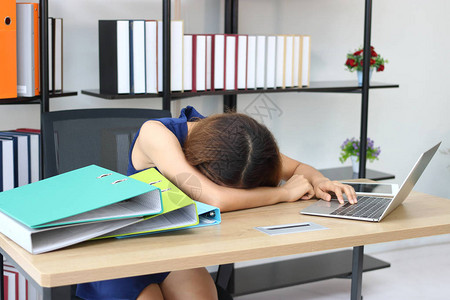疲劳过度的亚洲年轻商业妇女弯下头在办公图片