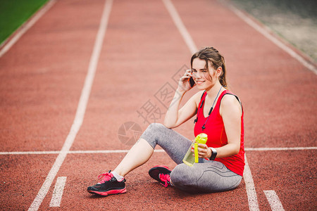 马尾辫在体育场的红色跑步赛道上锻炼后坐着休息图片