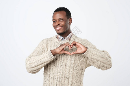 微笑的非洲年轻人用孤立的白种手指来制造手心形图片