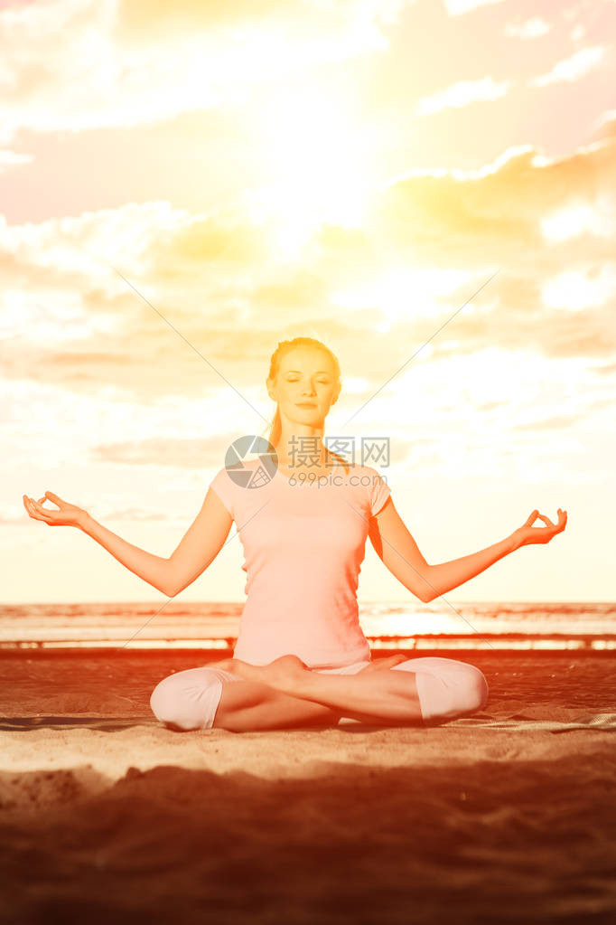 年轻漂亮的苗条女人在日出时在海滩上练习瑜伽日落时的瑜伽图片
