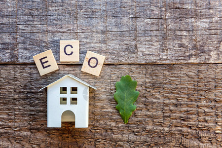 木制背景上刻有ECO字母的微型玩具模型屋生态村图片
