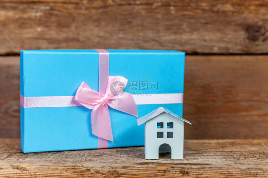 微型白色玩具屋和礼品盒在破旧的质朴木制背景上包裹着蓝纸图片