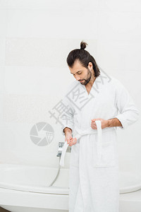 英俊的男人在白色的浴室里解开浴袍图片