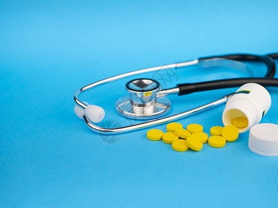 医生的黑色听诊器和黄色药丸和塑料白瓶医疗保健概念蓝色背景图片
