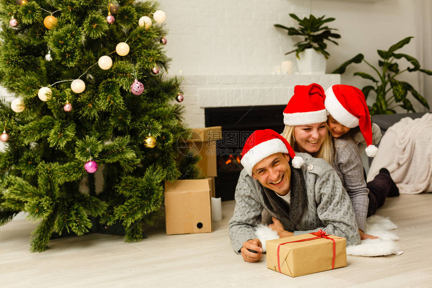 家庭戴着红色圣塔帽在圣诞树旁边图片
