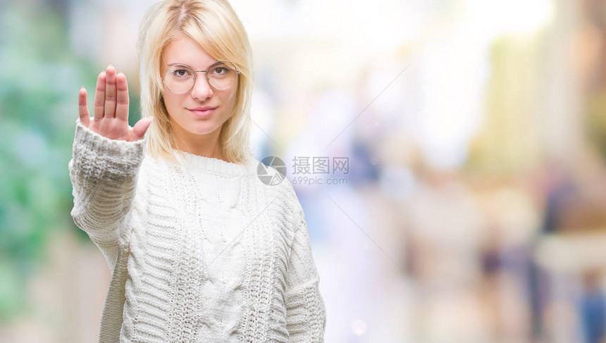 年轻漂亮的金发女郎穿着冬季毛衣和眼镜在孤立的背景下停止用手掌脸上带着消极和严肃的图片