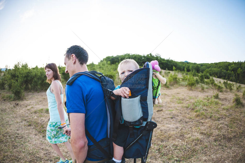 一家人带着孩子去旅行一个男人背着他的儿子在背包里和家人一起散步这个男孩正和他的父图片