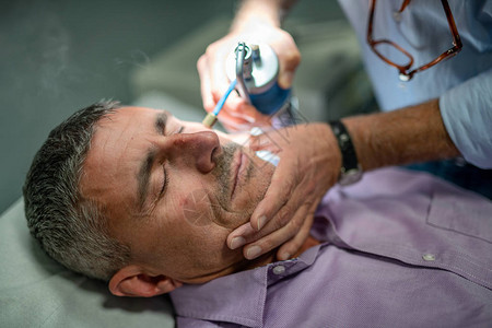 50年代白人男子在美容诊所接受激光面部治疗的特写镜头接受局部冷图片